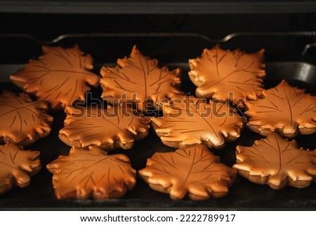 Gingerbread cookies with orange icing in the shape of fallen autumn leaves freshly baked out of the oven. Thanksgiving Day or Halloween festive background.