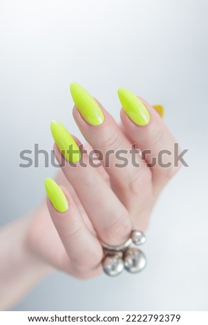 Female hand with long nails and neon yellow green manicure with bottles of nail polish