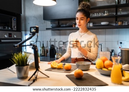 One woman young adult caucasian female making video or broadcast online as blogger about food preparation in the kitchen talking to her followers about ingredients and making process explain recipe