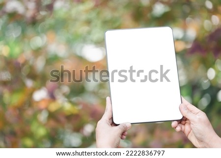 Woman hand holds modern white screen tablet on floral background, Travel concept. Business office ideas. Choice of travel. Copy space. Online store. technology digital cyberspace. web network.