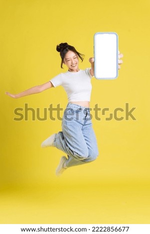 full body image of young Asian girl holding phone with cheerful face on yellow background Royalty-Free Stock Photo #2222856677