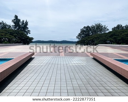 Floor tiled walkway to the ocean and trees on both sides.