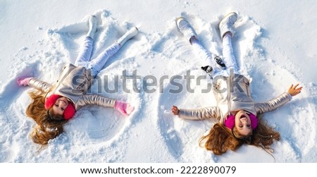 Winter angels. Happy kids girls on make snow angel wings. Two children making snow angel, lying on snow. Excited child playing on winter background. Winter games with snow for kids.