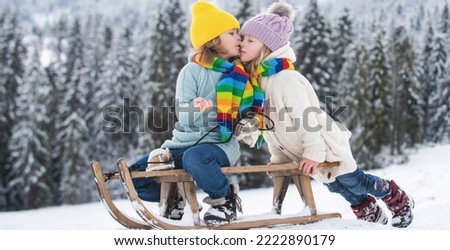 Outdoor kids little boy and girl kiss on winter outdoors. Happiness and kids love. Little couple on a sleigh kissing. Child friends kissed.