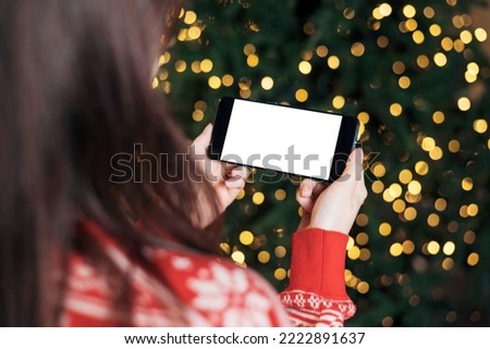 Woman holding smartphone with mock-up screen horizontal position on Christmas bokeh background. Mobile Phone in hand. Close up hands.
