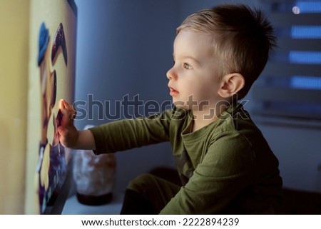 Children's addiction to television and cartoons. The boy touches a TV screen. A close-up shot of a kid sitting right in front of the TV and staring at a cartoon. Entertaining a child before bed time