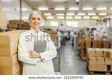 Portrait of food factory inspector leaning on boxes with merchandise and smiling at the camera.
