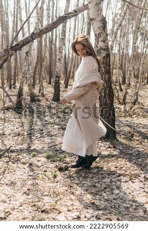 Beautiful girl in a white dress and a beige coat in a spring birch grove