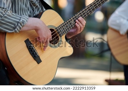 Man playing acoustic bass guitar at outdoor event, close up view to wooden guitar neck. Right handed bass player man playing four strings bass guitar, very nimble fingers of street music artist Royalty-Free Stock Photo #2222913359