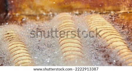 Cooking spiral fried potato in boiling oil, rich in fat and calories fast food, unhealthy but very delicious dish on street food festival. Close up spiral potato tornado cooking in fryer Royalty-Free Stock Photo #2222913387