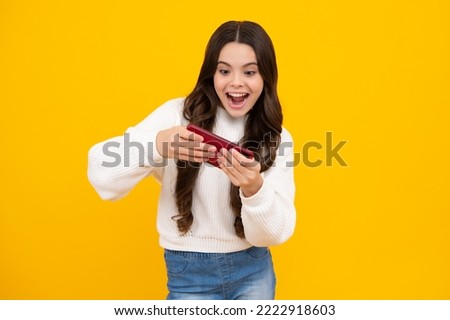 Excited teenager girl use smart phone, share social media, chatting by mobile phone wear stylish casual trendy clothes isolated over yellow background. Child with smartphone.