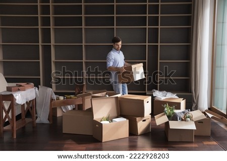 Millennial man carrying packed cardboard boxes with personal belongings to unfurnished cozy living room during move-in relocation day to new first own apartment. Tenancy, bank mortgage, independence Royalty-Free Stock Photo #2222928203