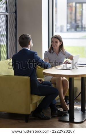 Two young business partners shake hands making deal smiling feels satisfied express respect for collaboration seated at table in modern workspace. Job interview pass successfully applicant get hired