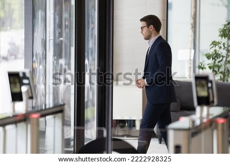 Millennial businessman in formal suit leaving office building area, passes through doorway, security gateway and electronic card reader, working day ended, going at lunch break in modern workplace Royalty-Free Stock Photo #2222928325