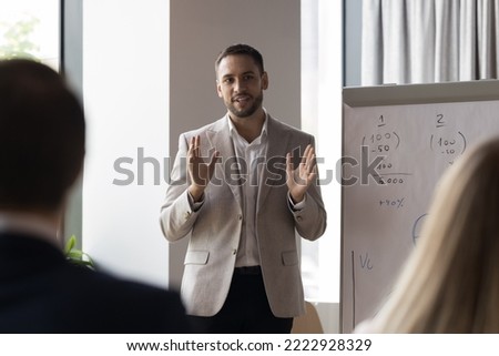 Business trainer makes speech during professional training in office boardroom, presents presentation on flip chart, provide information to participants, take part in seminar event in conference hall Royalty-Free Stock Photo #2222928329