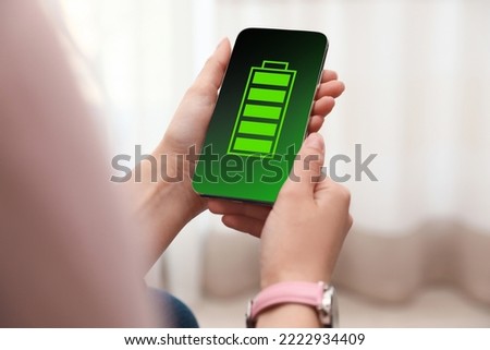 Young woman holding smartphone with fully charged battery indoors, closeup Royalty-Free Stock Photo #2222934409