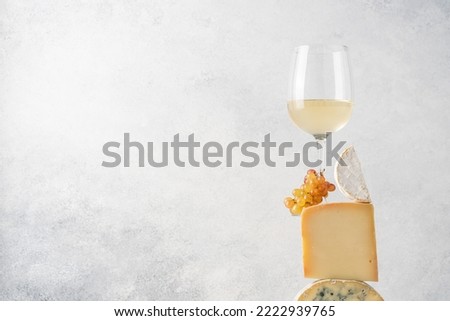 Cheese pyramid made of hard and soft blue cheese, Camembert. Balancing modern composition of set of cheeses, grapes and glass of white wine
