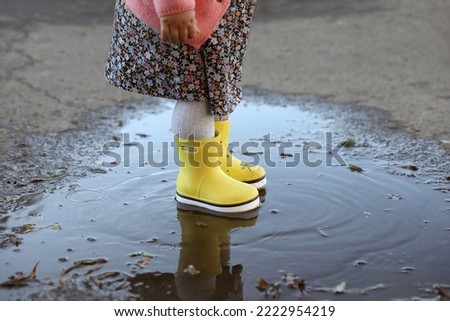 Little girl wearing rubber boots standing in puddle outdoors, closeup. Autumn walk