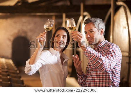 Couple tasting a glass of white wine in a traditional cellar surrounded by wooden barrels. Royalty-Free Stock Photo #222296008