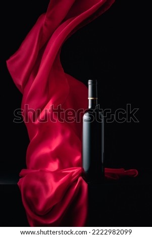 Вottle of red wine on a black background with flutters red cloth. Copy space.