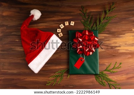 Handwrapped Christmas Gift on green  over a wood backdrop with  letters with a Santa hat. Aerial view, horizontal shot, copy space.