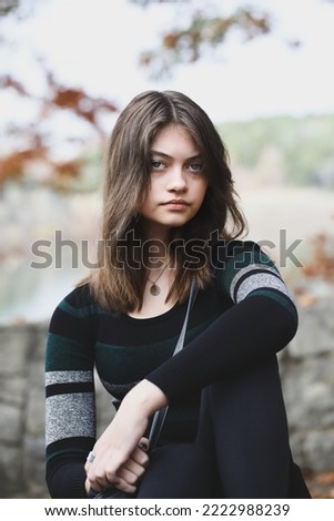 Beautiful brunette young woman looking into the camera with serious expression surrounded by outdoor autumn colors. Selective focus with blurred background.