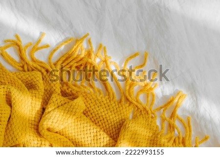 Bedding with a yellow knitted plaid. Cozy background with copy space. Hygge concept.