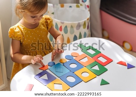 A little girl playing with wooden shape sorter toy on the table in playroom. Educational boards for Color and Shapes sorting for toddler. Learning through play. Developing Montessori activities. Royalty-Free Stock Photo #2222993165