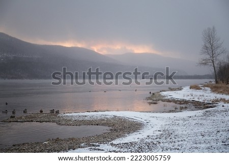 Winter landscape at sunset - river, ice on the shore, mountains in the background