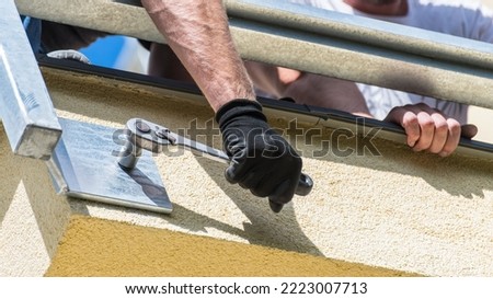 Bolting by ratcheting socket wrench. Fixing metal construction into building wall. Hand anchoring steel framework to concrete. Workers mounting balcony or terrace protective guard rails. Bottom view. Royalty-Free Stock Photo #2223007713