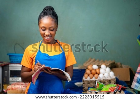 image of beautiful african lady with a book, food products sorrounded her- shopkeeper taking stock