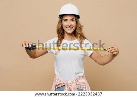 Young surprised employee laborer handyman woman wear white t-shirt helmet use show hold tape-measure isolated on plain beige background Instruments accessories for renovation room Repair home concept