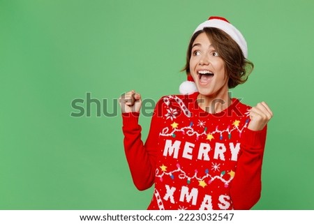 Side view merry young woman wear xmas sweater Santa hat posing do winner gesture celebrate clench fists isolated on plain pastel light green background Happy New Year 2023 celebration holiday concept Royalty-Free Stock Photo #2223032547
