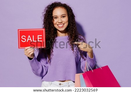 Young woman wear pullover hold in hand paper package bags after shopping point finger on card sign with sale title text isolated on plain pastel light purple background. Black Friday buy day concept