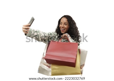 A young woman wearing knitted sweater holding a lot of shopping bag while doing selfies by smartphone. Happiness portrait of shopaholic girl in new year sale season.