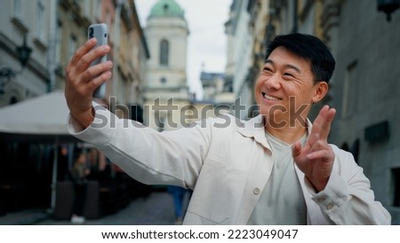 Joyful adult male tourist holding smartphone looking at screen taking pictures on webcam happy man blogger posing for photo photography using phone to shoot snapshot on mobile camera stands in city
