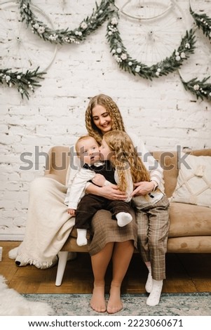 Merry Christmas and Happy Holidays. Young family photo at home. Mom hugs son and daughter enjoying time together. Mother embrace children. Decorated interior of a house. Closeup.