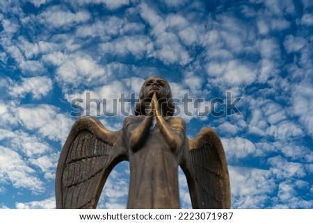 Detail of beautiful bronze statue of an angel with wings against the sky with white clouds. Beautiful angel with a blue sky background with space for text, close up