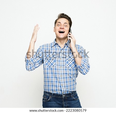 Young handsome man wearing blue plaid shirt gesturing and smiling while talking on the mobile phone over white background
