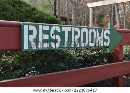 An arrowed green wooden sign with white lettering pointing to the restrooms.