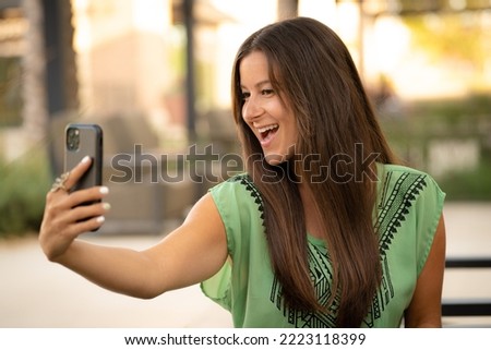 Beautiful Pretty Young Brunette Woman Taking Smiling Funny Selfie Photo Picture with Phone in Natural Soft Daylight at Mall Café Outside