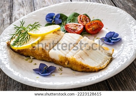 Fish dish - fried halibut with lemon and fresh vegetables on wooden table 