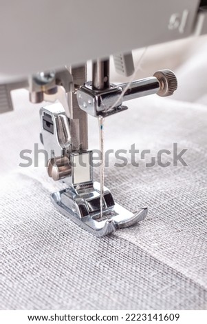 Modern sewing machine presser foot with linen fabric and thread, closeup, copy space. Sewing process clothes, curtains, upholstery. Business, hobby, handmade, zero waste, recycling, repair concept Royalty-Free Stock Photo #2223141609
