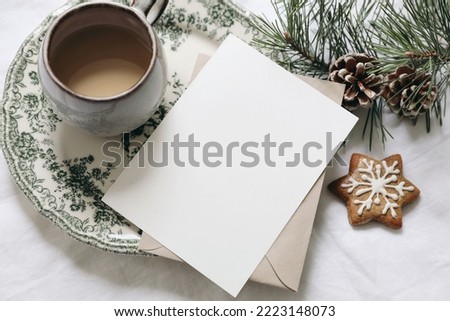 Christmas still life. Blank greeting card, invitation mockup.Gingerbread cookie, cup of coffee and pine tree branches. Floral green plate. White linen tablecloth with envelope. Winter festive flatlay.