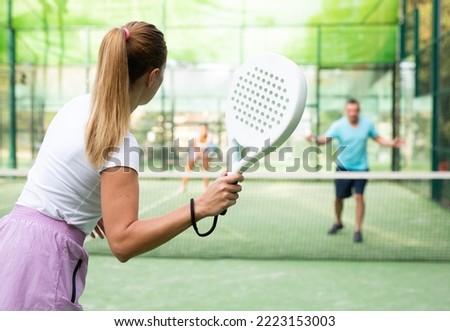 Rear view of woman playing paddle tennis match on outdoor court on blurred background of opponents. Sport and active lifestyle concept Royalty-Free Stock Photo #2223153003