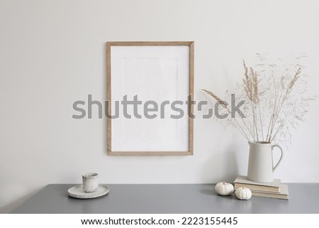 Autumn breakfast still life scene. ceramic jug with dry grass, cup of coffee. White little pumpkins, grey table. Blank wooden picture frame mockup. Scandinavian interior, boho home. Thanksgiving decor