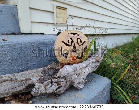 A pumpkin decoration sitting on a piece of driftwood on a stair.