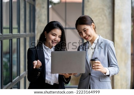Two pretty young Asian businesswomen standing to discuss working on investment projects and planning strategies together at the office. brainstorming concept.