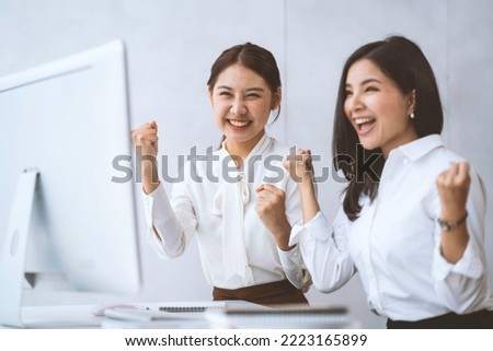 Two Asian businesswomen rejoice at their success in business and raise their hands in front of their laptop computers. Success in starting an online business.yes Royalty-Free Stock Photo #2223165899