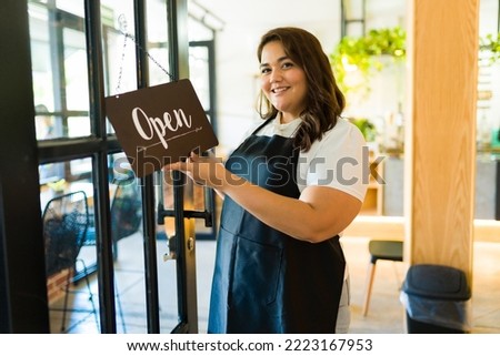 Portrait of a woman business owner smiling while putting an open sign on her restaurant or coffee shop 